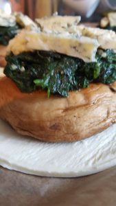 Raw pastry circle with mushroom spinach and stilton on top