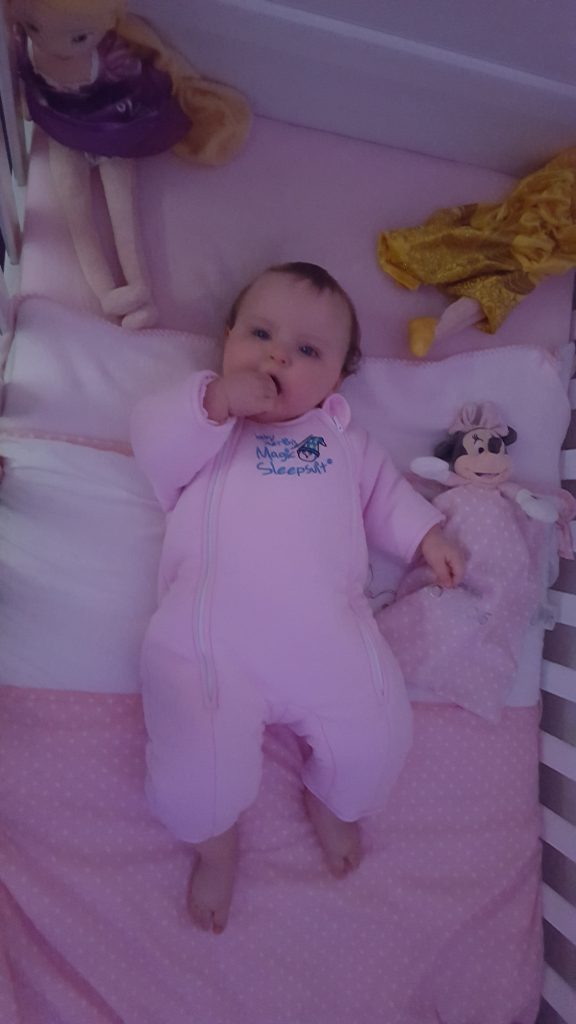 Baby lying in cot wearing pink magic sleepsuit