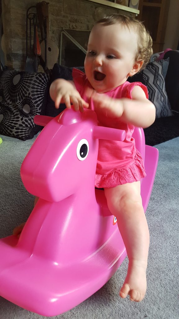 Alyssa in a pink dress riding a pink plastic rocking horse