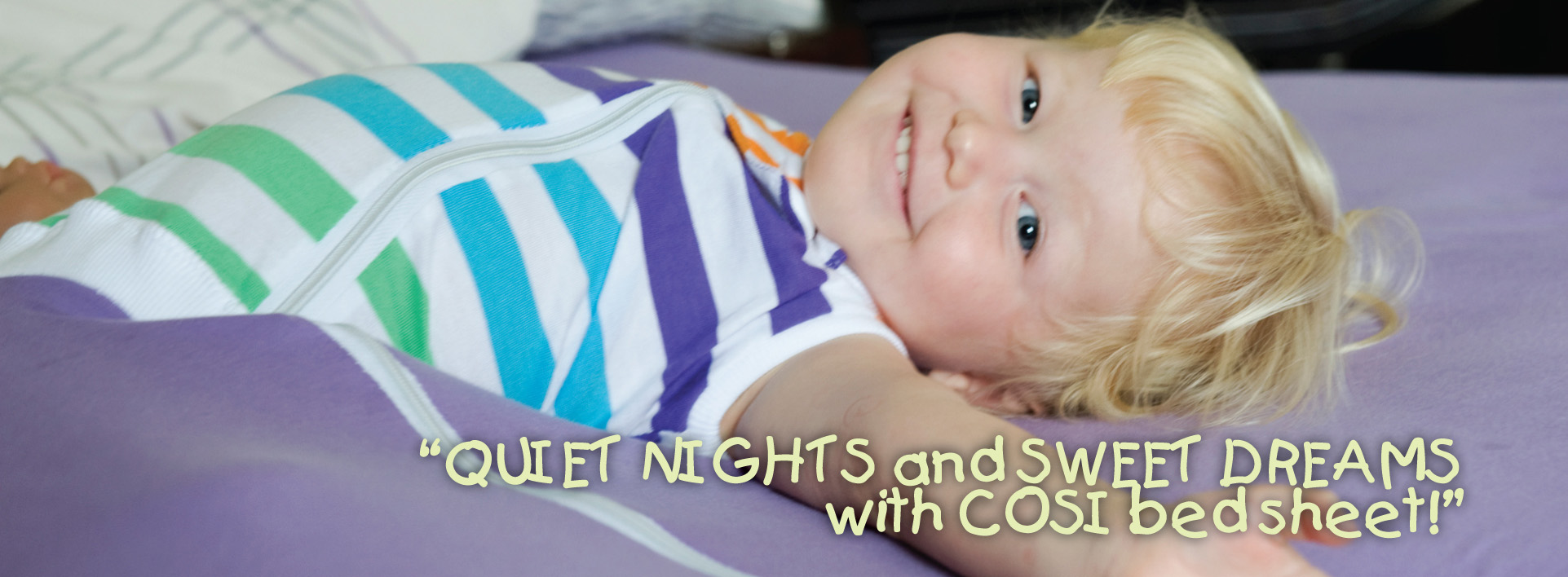 little blond boy lying down in a cosi blanket smiling at camera