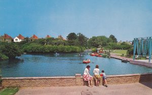 boating lake in a park. people stood eating ice lollies