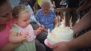 alyssa blowing candles on a cake out being held by Katie and  nanny in the background