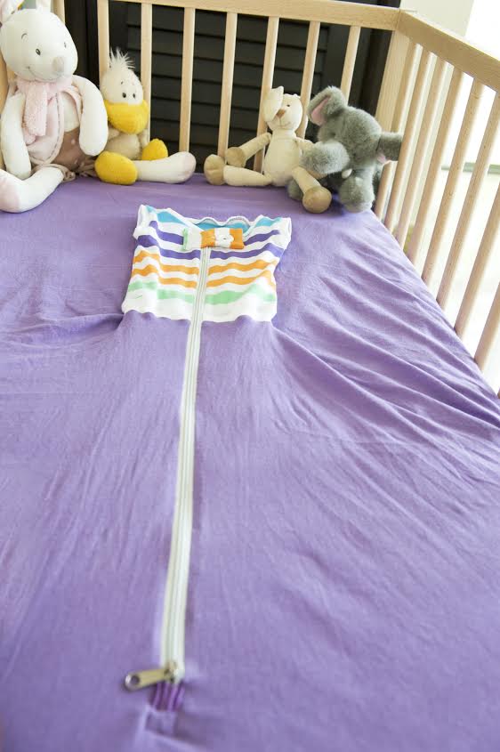 purple bed sheet with striped jacket in a cot with cuddly toys