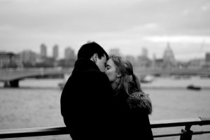 Man and woman in black and white kissing on a bridge