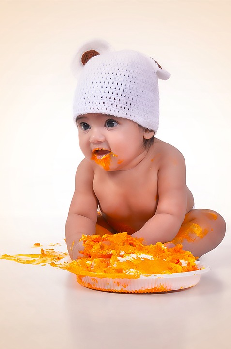 baby in a hat covered in orange food