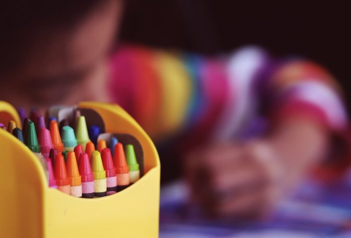 pack of crayons in the front a child colouring and blurred in the back