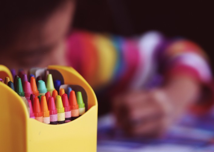 pack of crayons in the front a child colouring and blurred in the back