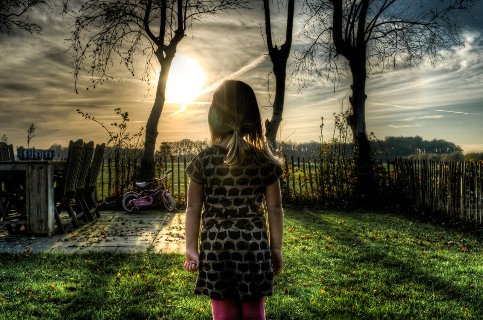 girl facing towards sunset with trees and fence in front of her