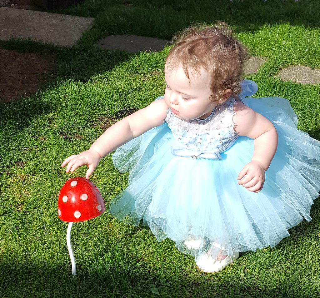 alyssa in a blue poofy dress reaching down to touch a toadstool