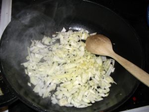 Onions frying in a large saucepan with a wooden spoon on the side