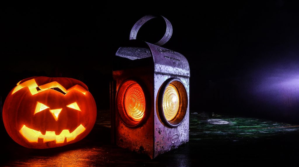 a carved pumpkin lit up with an old style lantern next to it lit too in drkness