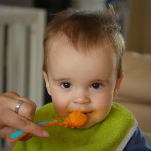 child with a spoon at mouth with orange mush on it