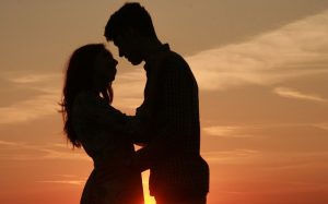 a couple in shadow with the sunset behind them about to kiss