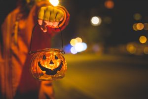 little girls arm holding a tiny glass pumpkin lantern with lights in the background