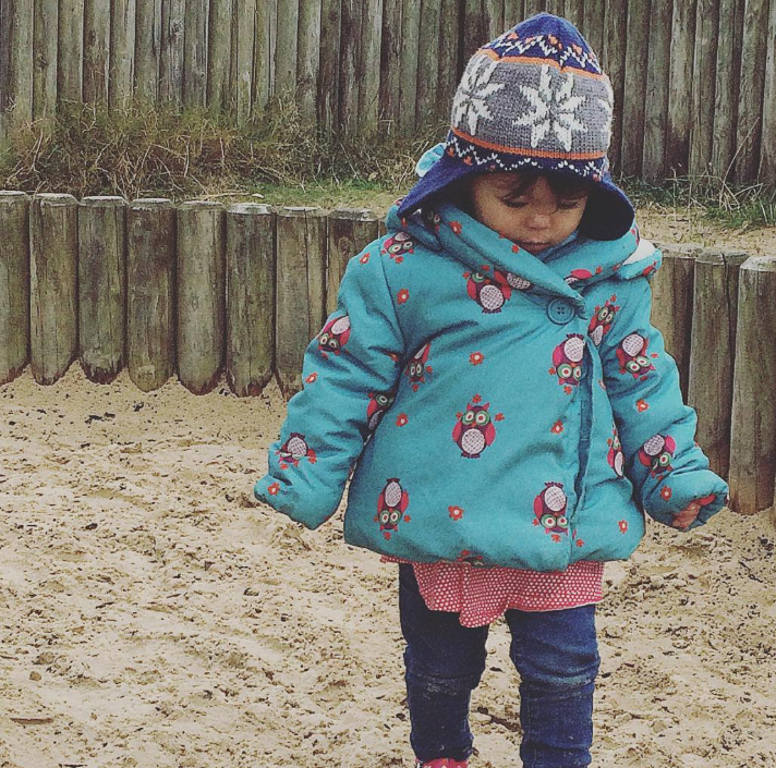 little girl in jeans blue coat and woolen hat walking along sand