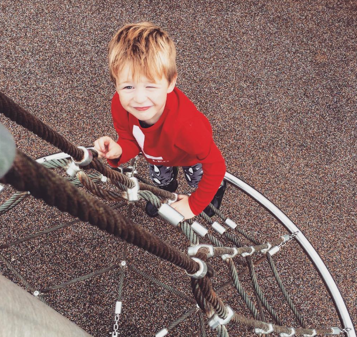 little boy climbing up a rope climb looking up at the camera