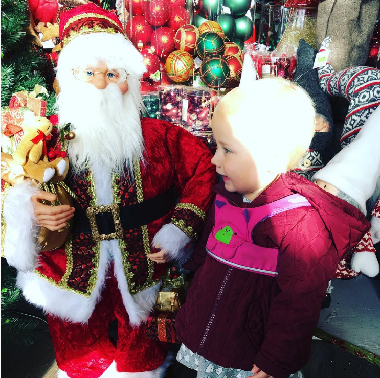 little girl smiling next to a santa figurine and baubles