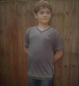 Rowan leaning against a fence, arms behind his back wearing a grey/blue coloured t-shirt