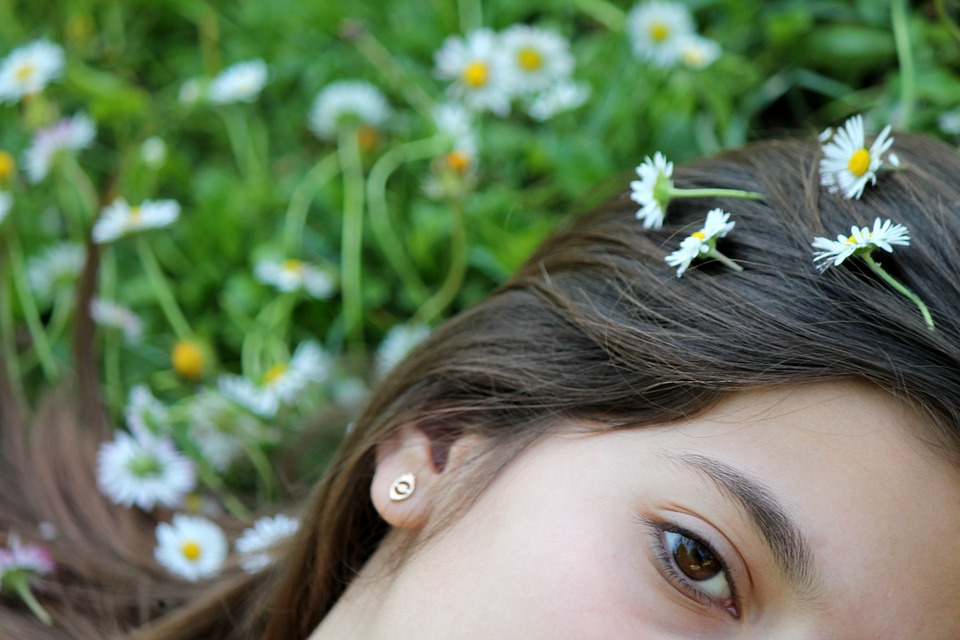 a young girl lying in daisys looking at the camera with a few daisys in her dark hair
