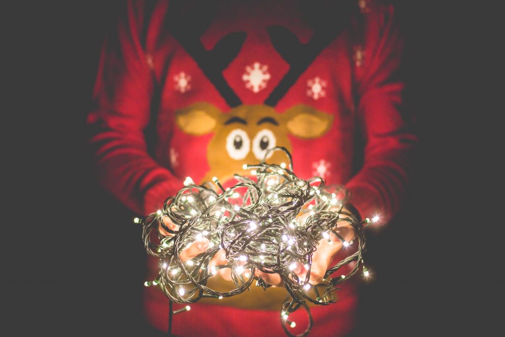 person in rudolph jumper holding a ball of christmas lights