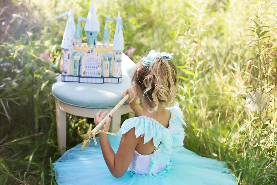 little girl in a princess dress next to a play castle sat in a sunny field