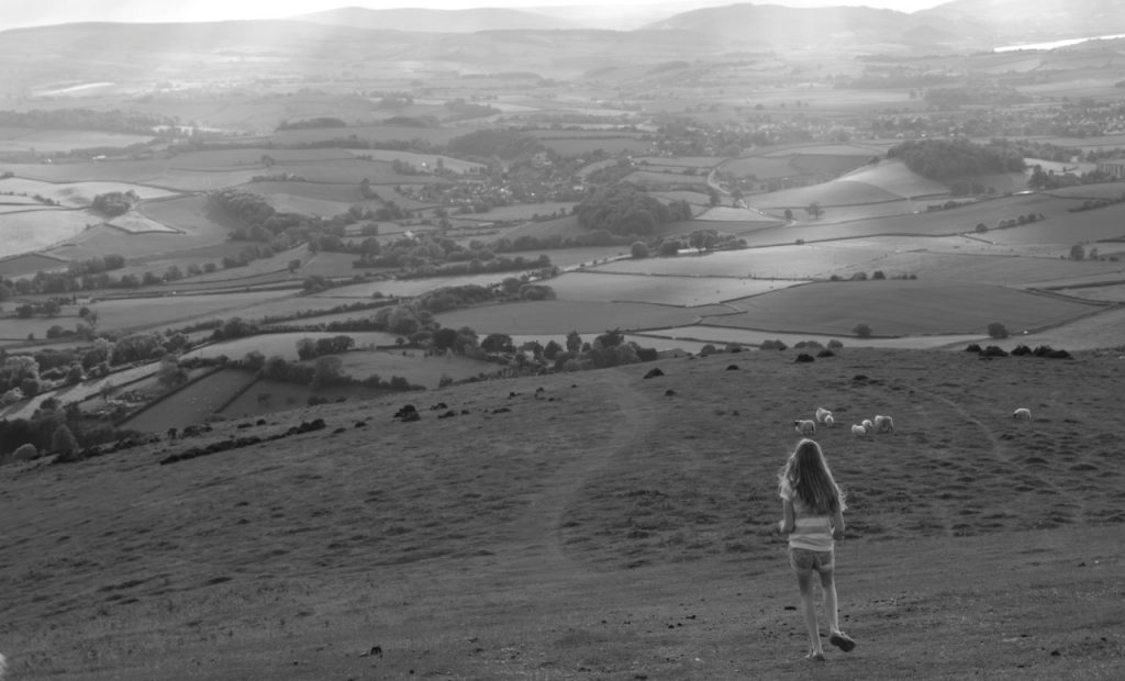 a black and white of a girl looking down over countryside
