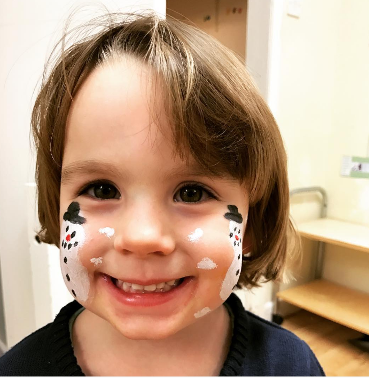 Brunette little girl smiling at the camera with a snow man face painted on each cheek