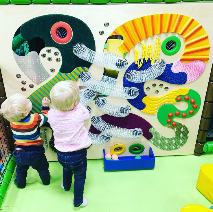 2 little blonde haired toddlers playing with an activity wall