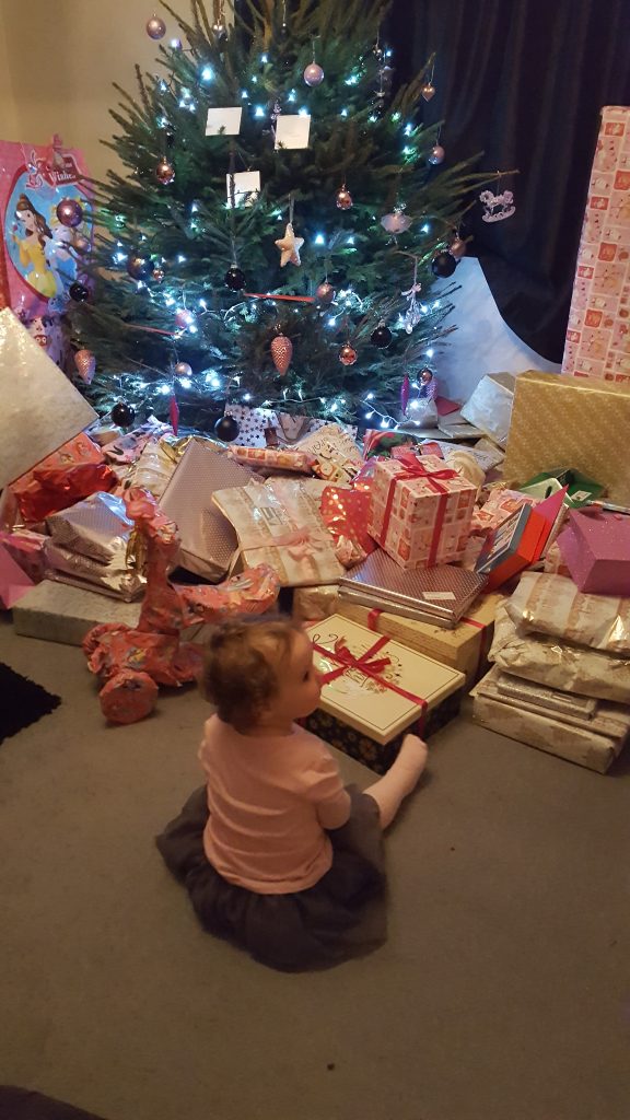 Alyssa sat in front of a lit chriistmas tree with all the presents in front of her
