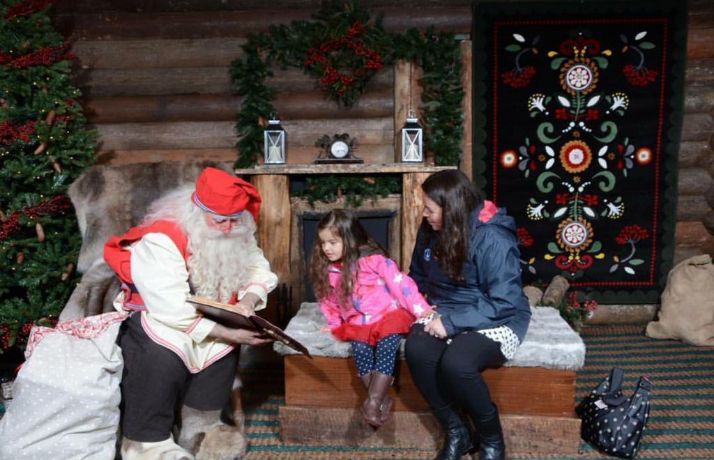 little girl sat on a bench looking at a book with Santa and her mummy sat next to her