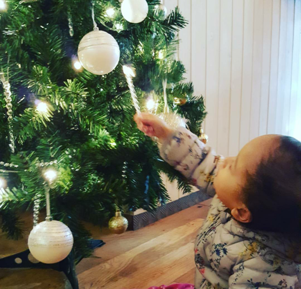 little child holding an icicle decoration looking up at a lit tree