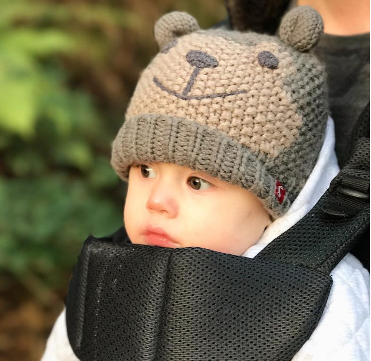 little baby in a body carrier in a white coat and a knitted bear hat with ears