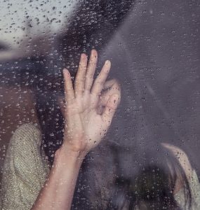 girl woman crying at a window with rain on it and hand on window