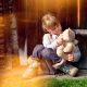 a little girl sat playing outside with her teddy against a wooden door on grass with sun shining down