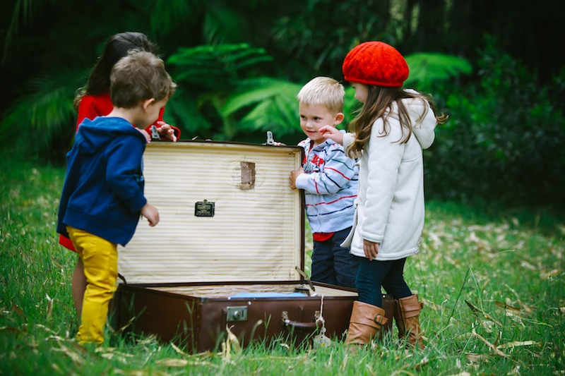 4 children gathered round and open old empty suitcase dressed in hats and coats in the middle of a green field