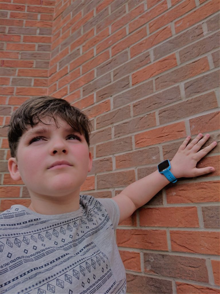 rowan leaning against a red brick wall with his hand and the blue kurio watch on it