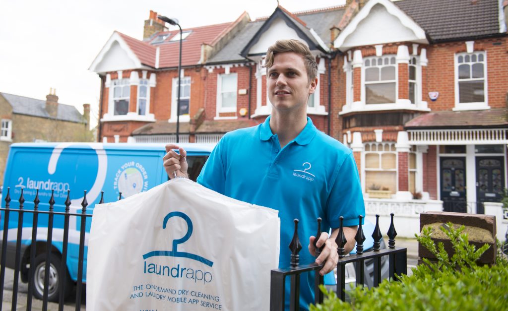 a man in a light blue polo shirt holding clean laundry walking up a path with a metal fence and brick houses behind