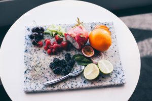 a white table with a grey marble chopping board on and an array of fruit with a knife as well