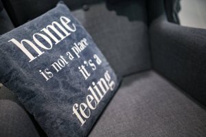blue cushion on a grey chair with white writing on saying "home is not a place it's a feeling"