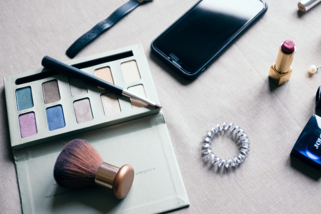 flat lay on white wood of makeup and a phone