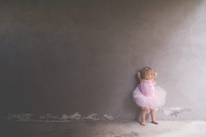 little blonde toddler leaningagainst a grey wall with her hands behind her head wearing a pink tutu