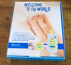 a johnsons box with a mums hand holding a baby's foot with the top toe toe bottles and logo pictured below all on a wooden table