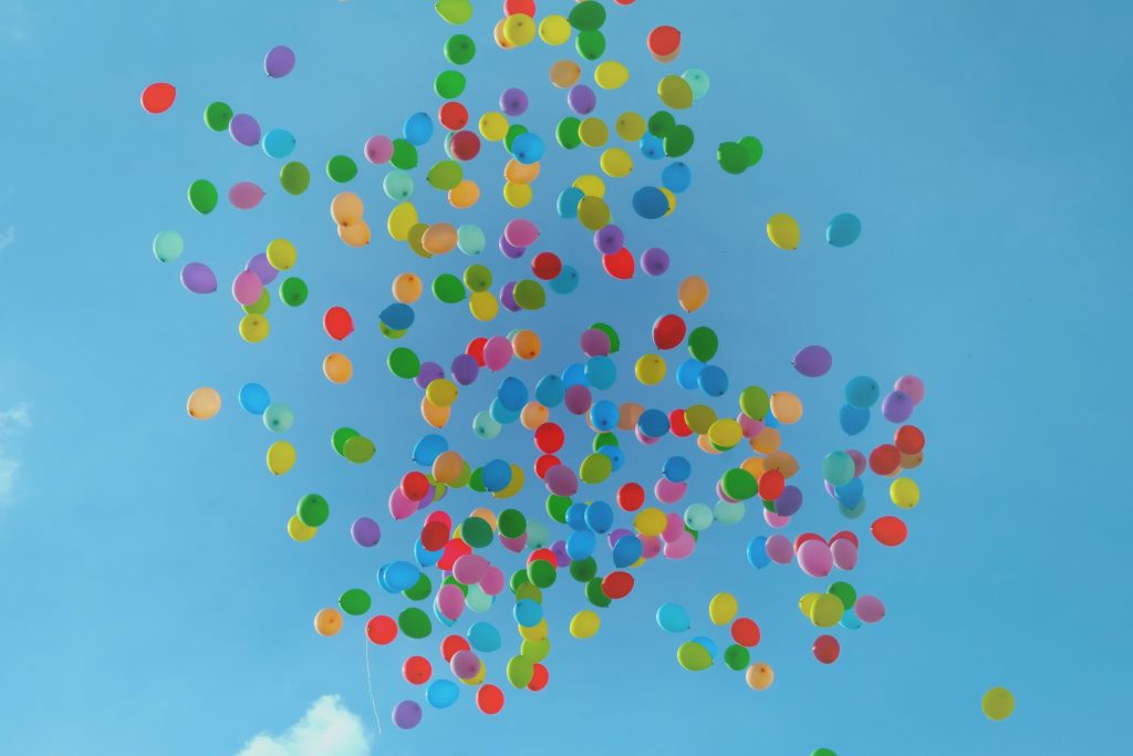 hundreds of balloons in every colour of the rainbow up high in the clear blue sky floating away