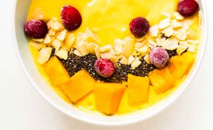 a white bowl with a yellow smoothie inside topped with fruits and nuts