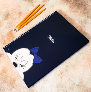 a navy blue minnie mouse a4 notepad with minnie mouse on the front and 3 orange pencils next to it