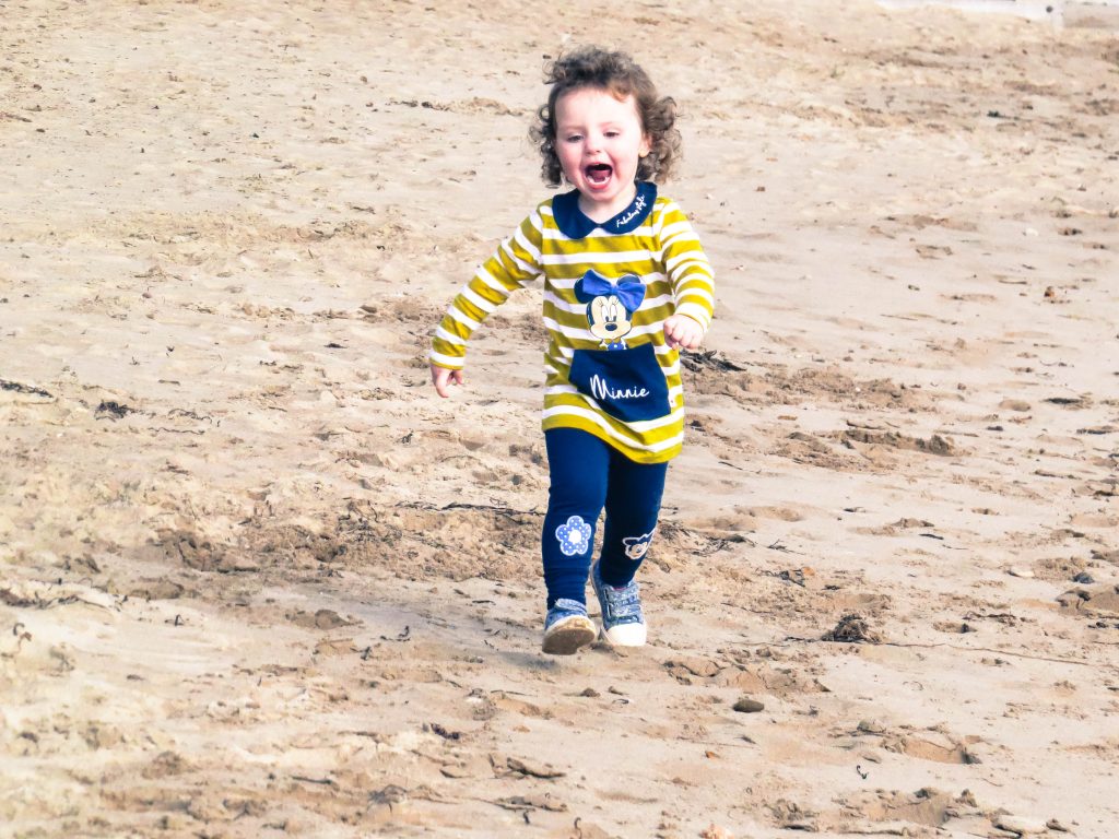 alyssa running up a beach wearing the minnie mouse outfit and laughing as she runs