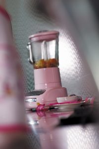pink kitchen blender with fruit in on a grey countertop