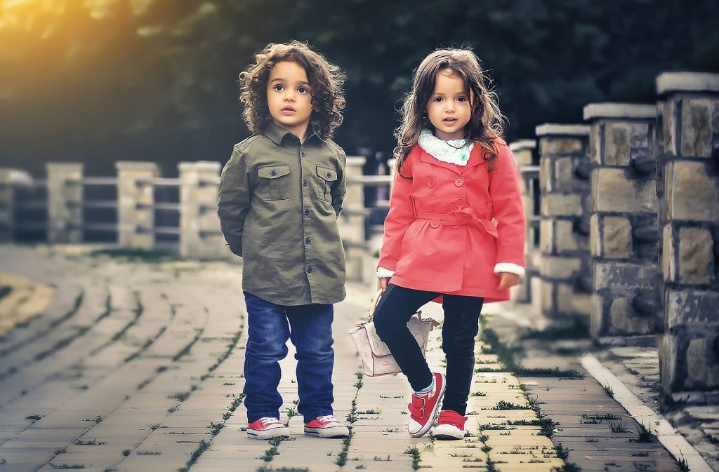 two children on a pavement in coats looking at the camera