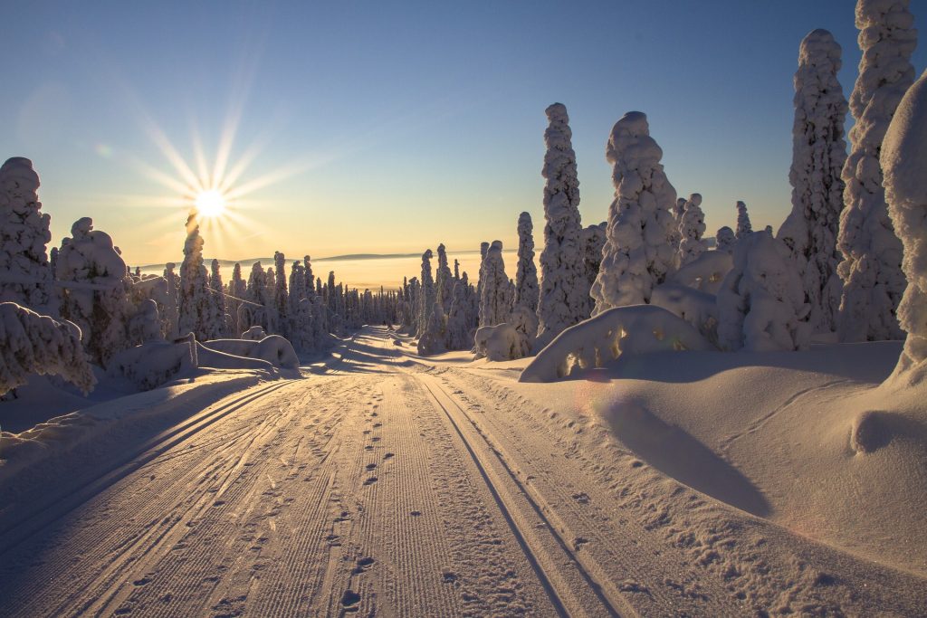 a snowy landscape with blue sky and the sun rising and shining