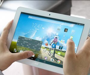 a pair of hands holding a white tablet on the main screen is the time and a blue sky and green grass picture
